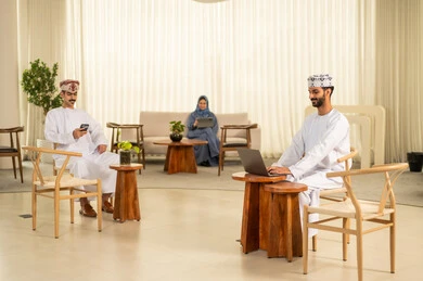 Management of business affairs and organization, teamwork and collaboration, companies and offices in the Kingdom of Saudi Arabia, an Arab Gulf Omani team consisting of a man wearing a thobe and a headscarf and a woman in a blue abaya, using a laptop and a tablet, gestures of engagement and focus.
