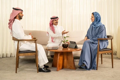 Developing plans and achieving the company's goals, collaborating and participating in completing tasks, a Gulf Arab Saudi team consisting of two men wearing traditional attire and a headscarf, and a veiled woman wearing a blue abaya sitting in front of a tablet.