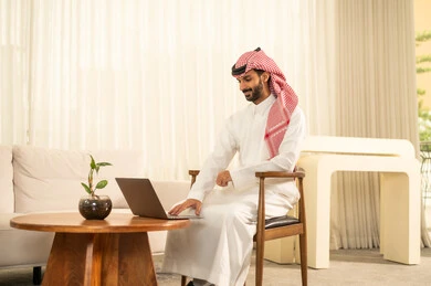 دمج التقنيات الحديثة و المتطورة مع العمل, إعداد و مراجعة تقارير الأداء، دراسة جدوى الأعمال، استخدام اللابتوب لإرسال البريد الإلكتروني، مهن و أعمال مكتبية إدارية, رجل عربي خليجي سعودي يرتدي الزي التقليدي والشماغ يجلس على المكتب امام جهاز اللابتوب