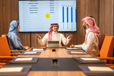 Task management and division, a Saudi Gulf Arab team conducting a business meeting inside the company's conference room, explaining and analyzing charts, integrating modern technological devices with office work, studying statistical data sheets, developing projects and investments.