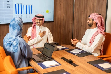Task management and division, a Saudi Gulf Arab team conducting a business meeting inside the company's conference room, explaining and analyzing charts, integrating modern technological devices with office work, studying statistical data sheets, developing projects and investments.