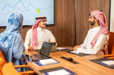 Task management and division, a Saudi Gulf Arab team conducting a business meeting inside the company's conference room, explaining and analyzing charts, integrating modern technological devices with office work, studying statistical data sheets, developing projects and investments.