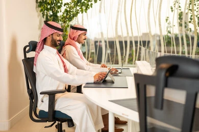 Understanding and cooperation among colleagues to achieve the company's goals, the concept of business management, completing tasks through modern devices, following up on the work strategy, Arab Gulf colleagues from Saudi Arabia sitting in the office and working on the laptop and tablet.