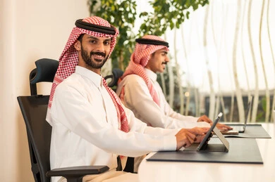 Accomplishing tasks through modern devices, understanding and cooperation among colleagues to achieve the company's goals, the concept of business management, following up on the work strategy, Arab Gulf Saudi colleagues sitting in the office and working on the laptop and tablet.