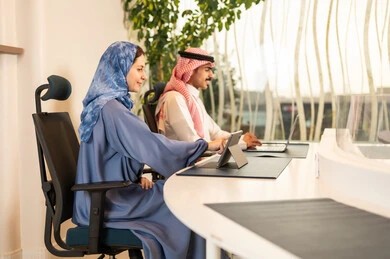 مفهوم إدارة الأعمال، التفاهم و التعاون بين الزملاء لتحقيق أهداف الشركة، إنجاز المهام عبر الأجهزة الحديثة, متابعة إستراتيجية العمل، زملاء عمل عرب خليجيين سعوديين يجلسون داخل المكتب و يعملان على اللابتوب و التابلت