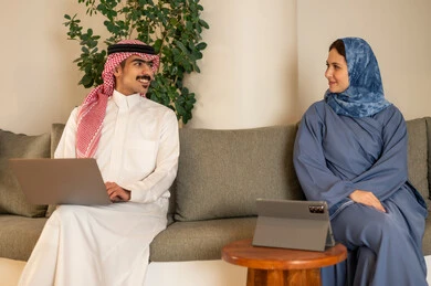 The concept of business management, discussing ideas and exchanging opinions, understanding and cooperation among colleagues to achieve the company's goals, completing tasks using modern devices, following up on the work strategy, Arab Gulf colleagues from Saudi Arabia sitting in the office and working on laptops and tablets.