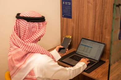 ارسال بريد إلكتروني عبر الكمبيوتر، التواصل مع العملاء عن بعد، دمج التقنيات الحديثة و المتطورة مع العمل, مهن و أعمال مكتبية إدارية, رجل عربي خليجي سعودي  يرتدي الزي التقليدي والشماغ يجلس على المكتب امام جهاز اللابتوب و يتحدث عبر المحمول, تعابير وايماءات الاندماج