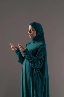 الدعاء لله بخضوع ورجاء مستمر، طلب العون والرغبة في تحقيق الأمنيات, بورترية لامراة عربيه خليجه عربيه سعودية ترتدي العباءة و الحجاب تنظر إلى الأعلى ترفع يديها بخشوع واستعطاف, خلفية رمادية