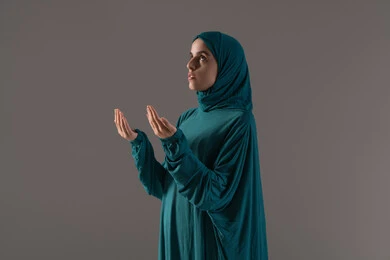 اللجوء إلى الله بالدعاء والتوسل بخشوع، طلب العون والرغبة في تحقيق الأمنيات, بورترية لامراة عربيه خليجه عربيه سعودية ترتدي العباءة و الحجاب تنظر إلى الأعلى ترفع يديها بخشوع واستعطاف, خلفية رمادية