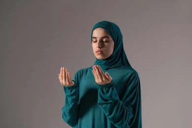 التذلل والتضرع لله لطلب المعونة، طلب العون والرغبة في تحقيق الأمنيات, بورترية لامراة عربيه خليجه عربيه سعودية ترتدي العباءة و الحجاب تنظر إلى الأعلى ترفع يديها بخشوع واستعطاف, خلفية رمادية