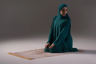 الشعور بالخشوع والطمأنينة، أداء الفرائض الدينية الإسلامية, إقامة الصلاة على وقتها, مفهوم أركان الإسلام، بورترية لامراه عربيه خليجيه سعودية تجلس على سجادة الصلاة تقوم بالتسليم في ختام الصلاة، العبادة والتقرب إلى الله، خلفية رمادية