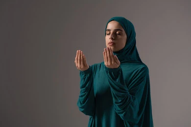 التضرع إلى الله بصدق وتواضع، الدعاء والتوسل والاسترحام، طلب العون والرغبة في تحقيق الأمنيات, بورترية لامراة عربيه خليجه عربيه سعودية ترتدي العباءة و الحجاب تنظر إلى الأعلى ترفع يديها بخشوع واستعطاف, خلفية رمادية