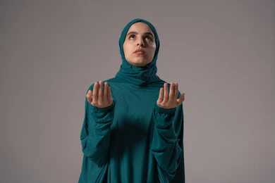 الطلب بترجي وتذلل من رب العباد، الدعاء والتوسل والاسترحام، طلب العون والرغبة في تحقيق الأمنيات, التضرع إلى الله تعالى, بورترية لامراة عربيه خليجه عربيه سعودية ترتدي العباءة و الحجاب تنظر إلى الأعلى ترفع يديها بخشوع واستعطاف, خلفية رمادية