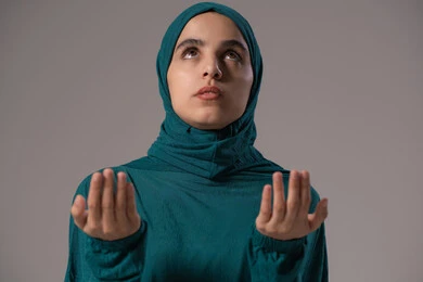 الدعاء والتوسل والاسترحام، طلب العون والرغبة في تحقيق الأمنيات, التضرع إلى الله تعالى, الطلب بترجي وتذلل من رب العباد, بورترية لامراة عربيه خليجه عربيه سعودية ترتدي العباءة و الحجاب تنظر إلى الأعلى ترفع يديها بخشوع واستعطاف, خلفية رمادية