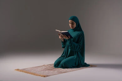 التفكر والخشوع في التقرب إلى الله، التقرب الى الله تعالى، بورترية لامراة عربيه خليجه عربيه سعودية ترتدي العباءة و الحجاب تجلس علي سجادة الصلاة و تقرأ القرآن الكريم، المناسبات الدينية والأعياد الإسلامية، خلفيه رمادية