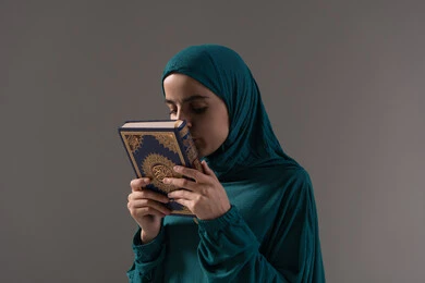 تعظيم المصحف الشريف، حب كتاب الله و تقبيله, بورترية لامراة عربيه خليجه عربيه سعودية ترتدي العباءة و الحجاب تمسك القرآن الكريم بيديها، الاجتهاد في العباده والطاعة، خلفية رمادية