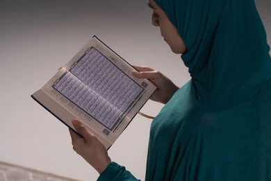 الانغماس بخشوع في الطاعات، التقرب الى الله تعالى، بورترية مقرب من الجانب لامراة عربيه خليجه عربيه سعودية ترتدي العباءة و الحجاب تقرأ القرآن الكريم، المناسبات الدينية والأعياد الإسلامية، خلفيه رمادية