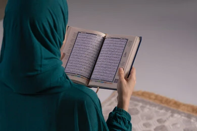 التدبر والخشوع في العبادة، التقرب الى الله تعالى، بورترية مقرب من الخلف لامراة عربيه خليجه عربيه سعودية ترتدي العباءة و الحجاب تقرأ القرآن الكريم، المناسبات الدينية والأعياد الإسلامية، خلفيه رمادية