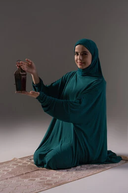 Preparing for the arrival of the blessed Ramadan, the joy of the coming month of goodness, a portrait of a Saudi Gulf Arab woman wearing a hijab and an abaya sitting on a prayer rug holding a decorative metal lantern in her hand, celebrating Islamic religious occasions, expressions of happiness and joy, gray background.