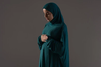 The concept of the pillars of Islam and faith, obedience and worship, and drawing closer to God through the performance of acts of worship, a portrait of an Emirati Gulf Arab woman wearing a hijab and abaya standing on a prayer rug performing the obligatory prayers, a Saudi woman supplicating and being humble during prayer, Islamic themes and worship, white background.