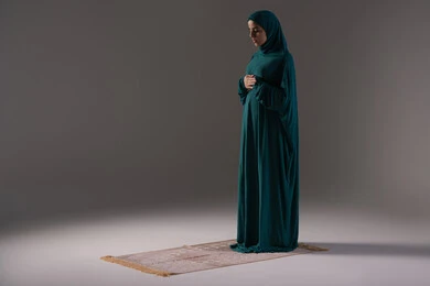 تطهير القلب بالتضرع لرب العالمين، الطاعة والعبادة والتقرب إلى الله عن طريق القيام بالعبادات، بورترية لإمرأة عربية خليجية اماراتية ترتدي الحجاب والعباءة تقف على السجادة تقوم بأداء الفرائض ، سيده سعودية تقوم بالتضرع والخشوع أثناء الصلاة, اسلاميات وعبادة، خلفية بيضاء