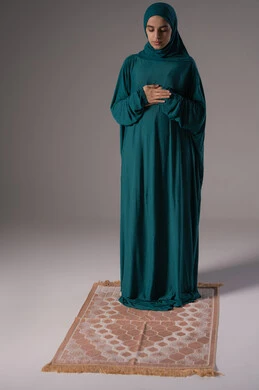 Obedience, worship, and drawing closer to God through performing acts of worship, a portrait of an Emirati Gulf Arab woman wearing a hijab and abaya standing on a prayer rug performing the obligatory prayers, a Saudi woman supplicating and being humble during prayer, self-improvement by humbling oneself before the Lord of the worlds, Islamic themes and worship, white background.