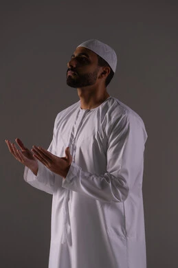 طلب العون والرغبة في تحقيق الأمنيات، التضرع إلى الله تعالى, بورتريه لرجل عربي خليجي إماراتي يرتدي الكندورة و القبعة البيضاء يرفع يديه بخشوع واستعطاف, الوقوف بإيماءات الدعاء والتوسل والاسترحام, الطلب بترجي وتذلل من رب العباد, خلفية بيضاء
