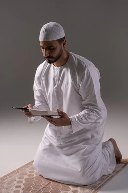 التدبر في معاني القرآن والتفكر بها، الشعور بالخشوع والطمأنينة، بورتريه لرجل عربي خليجي إماراتي يرتدي الكندورة والطاقية البيضاء يجلس على سجادة الصلاة يقوم بقراءة المصحف الشريف، الإكثار من ذكر الله تعالى من خلال الاستغفار والدعاء، الاجتهاد في العبادة، التقرب الى الله في شهر رمضان، خلفية بيضاء