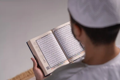 التأمل في معاني آيات القرآن الكريم، الشعور بالخشوع والطمأنينة، بورتريه  مقرب من الخلف لرجل عربي خليجي إماراتي يرتدي الكندورة والقبعة البيضاء يقوم بقراءة المصحف الشريف، الإكثار من ذكر الله تعالى من خلال الاستغفار والدعاء، الاجتهاد في العبادة، التقرب الى الله في شهر رمضان، خلفية بيضاء