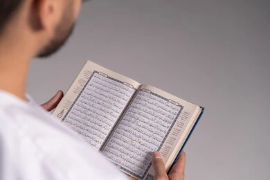 الاجتهاد في العبادة، الشعور بالخشوع والطمأنينة، تدبر آيات القران الكريم، بورتريه مقرب لرجل عربي خليجي إماراتي يرتدي الكندورة يقوم بقراءة المصحف الشريف، الإكثار من ذكر الله تعالى من خلال الاستغفار والدعاء، التقرب الى الله في شهر رمضان، خلفية بيضاء