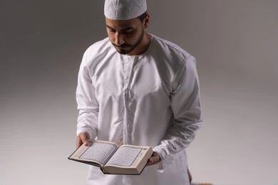 الشعور بالخشوع والطمأنينة، تدبر آيات القران الكريم، بورتريه لرجل عربي خليجي إماراتي يرتدي الكندورة والقبعة البيضاء يقوم بقراءة المصحف الشريف، الإكثار من ذكر الله تعالى من خلال الاستغفار والدعاء، الاجتهاد في العبادة، التقرب الى الله في شهر رمضان، خلفية بيضاء