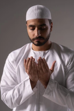 الإكثار من ذكر الله والدعاء والاستغفار، بورترية مقرب لشاب عربي خليجي اماراتي يرتدي الثوب الأبيض والطاقية يرفع يديه ويدعو الله بخشوع وتضرع، التقرب الى رب العالمين في شهر رمضان المبارك، الاجتهاد في العبادة واداء الفرائض الدينية، خلفية رمادية