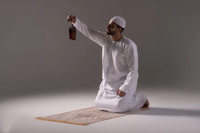 المناسبات الدينية والأعياد الإسلامية، أجواء السكينة والروحانية، بورترية لرجل عربي خليجي إماراتي يرتدي الكندورة البيضاء والطاقية يجلس على سجادة الصلاة يحمل بيدية فانوس معدني ينظر إليه، الإستعداد لقدوم شهر رمضان المبارك ، العبادة والتقرب إلى الله، خلفية رمادية المناسبات الدينية والأعياد الإسلامية، أجواء السكينة والروحانية، بورترية لرجل عربي خليجي إماراتي يرتدي الكندورة البيضاء والطاقية يجلس على سجادة الصلاة يحمل بيدية فانوس معدني ينظر إليه، الإستعداد لقدوم شهر رمضان المبارك ، العبادة والتقرب إلى الله، خلفية رمادية