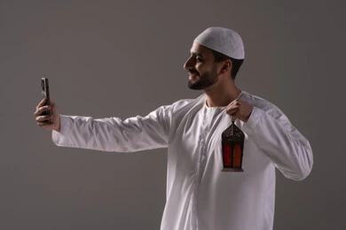أجواء رمضانية تعكس روح العبادة والتقوى، التقاط الصور لفانوس رمضان، العبادة والتقرب إلى الله، بورترية من الجانب لرجل عربي خليجي إماراتي يرتدي الكندورة البيضاء والطاقية يمسك بيده الهاتف المحمول، خلفية رمادية أجواء رمضانية تعكس روح العبادة والتقوى، التقاط الصور لفانوس رمضان، العبادة والتقرب إلى الله، بورترية من الجانب لرجل عربي خليجي إماراتي يرتدي الكندورة البيضاء والطاقية يمسك بيده الهاتف المحمول، خلفية رمادية