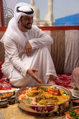 سفره تضم مجموعة من المأكولات المختلفة، مطاعم و كافيهات في الإمارات، مائدة مليئة بتشكيلة متنوعة من المأكولات، قضاء الأوقات الممتعة في الخارج, رجل عربي خليجي اماراتي يرتدي الكندورة و الغتره يجلس فى مجلس ارضي شعبي ، ايماءات السعادة و السرور