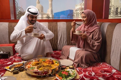 مطاعم و كافيهات في الإمارات، مائدة مليئة بتشكيلة متنوعة من المأكولات، قضاء الأوقات الممتعة في الخارج, رجل عربي خليجي اماراتي يرتدي الكندورة و الغتره يجلس فى مجلس ارضي شعبي يقوم بتناول صحن من الشوربة برفقة زوجته ، الإجتماع العائلي في المناسبات الدينيه السعيده مطاعم و كافيهات في الإمارات، مائدة مليئة بتشكيلة متنوعة من المأكولات، قضاء الأوقات الممتعة في الخارج, رجل عربي خليجي اماراتي يرتدي الكندورة و الغتره يجلس فى مجلس ارضي شعبي يقوم بتناول صحن من الشوربة برفقة زوجته ، الإجتماع العائلي في المناسبات الدينيه السعيده