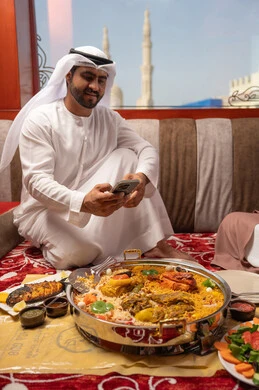 توثيق اللحظات الممتعة، رجل عربي خليجي اماراتي يرتدي الكندورة و الغتره يجلس فى مجلس ارضي شعبي حول مائدة الطعام ، التقاط صور تذكارية للمائدة عبر الهاتف المحمول توثيق اللحظات الممتعة، رجل عربي خليجي اماراتي يرتدي الكندورة و الغتره يجلس فى مجلس ارضي شعبي حول مائدة الطعام ، التقاط صور تذكارية للمائدة عبر الهاتف المحمول