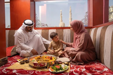 A Ramadan iftar table filled with delicious dishes and appetizers, restaurants and cafes in the United Arab Emirates, an Emirati Gulf Arab family dressed in traditional attire sitting in a popular family gathering on the floor around the dining table.