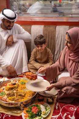 مائدة رمضان مليئة بالأطباق والمقبلات المختلفة, مطاعم و كافيهات في الإمارات العربية المتحدة، عائلة عربيه خليجيه اماراتية ترتدي الزي التقليدي تجلس فى مجلس ارضي شعبي العائلة حول مائدة الطعام
