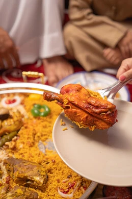 Healthy and delicious dishes, a metal tray filled with rice and spices, a close-up image of the hand of an Emirati Gulf Arab woman holding a plate of rice garnished with stuffed chicken.