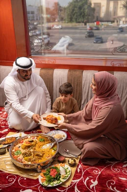 A diverse iftar during Ramadan includes dishes and appetizers, restaurants and cafes in the United Arab Emirates. An Emirati Gulf Arab family dressed in traditional attire sits in a popular ground seating area around the dining table.