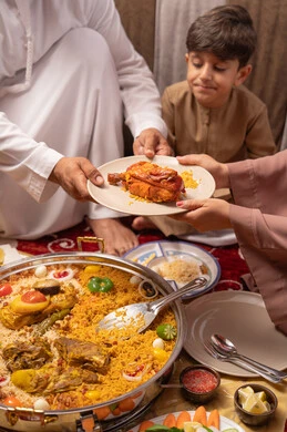 سفرة رمضان مليئة بالأطعمة والمقبلات الشهية , مطاعم و كافيهات في الإمارات العربية المتحدة، عائلة عربيه خليجيه اماراتية ترتدي الزي التقليدي تجلس فى مجلس ارضي شعبي العائلة حول مائدة الطعام