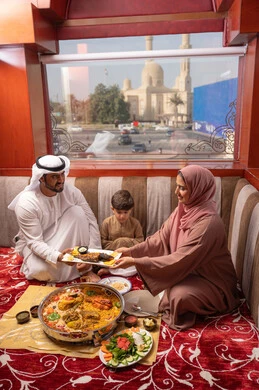 مائدة إفطار شهر رمضان مع أصناف متنوعة من الأطباق والمقبلات , مطاعم و كافيهات في الإمارات العربية المتحدة، عائلة عربيه خليجيه اماراتية ترتدي الزي التقليدي تجلس فى مجلس ارضي شعبي العائلة حول مائدة الطعام