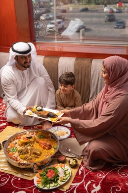 A rich Ramadan iftar filled with delicious dishes and appetizers, restaurants and cafes in the United Arab Emirates, an Emirati Gulf Arab family dressed in traditional attire sitting in a popular ground seating area around the dining table.