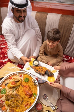The Ramadan iftar table features a variety of foods and appetizers, restaurants and cafes in the United Arab Emirates, a Gulf Arab Emirati family dressed in traditional attire sitting in a popular ground seating area around the dining table.