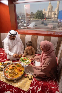 سفرة إفطار مليئة بأطباق من المأكولات والمقبلات الشهية في شهر رمضان المبارك, مطاعم و كافيهات في الإمارات العربية المتحدة، عائلة عربيه خليجيه اماراتية ترتدي الزي التقليدي تجلس فى مجلس ارضي شعبي العائلة حول مائدة الطعام