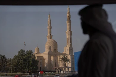 ايماءات الاندماج و التأمل، روحانيات ومعمار إسلامي، صورة ظلية من الخلف لرجل عربي خليجي إماراتي يرتدي الكندورة و الغتره يقف خلف النافذة يشاهد المسجد