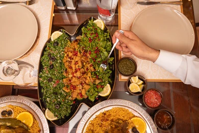 Skills in presenting dishes in Emirati cuisine, a Ramadan table filled with delicious foods, a close-up image of the hand of an Arab Gulf Emirati man having breakfast.
