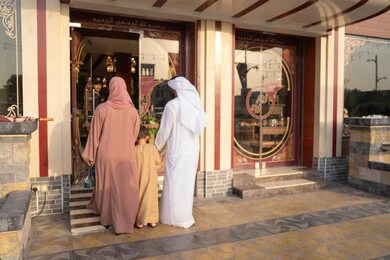 قضاء الأوقات الممتعة مع الأبناء، لحظات دخول عائلة عربية خليجية اماراتية إلى المطعم، صورة من الخلف لرجل عربي خليجي اماراتي يرتدي الكندورة و الدشداشة يسير برفقه زوجته و ابنة