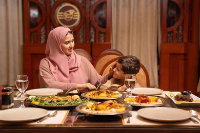 ام عربيه خليجيه اماراتية ترتدي العباءة و الحجاب تقوم بتناول الافطار برفقة ابنها، شهر الخير والبركة ، المأكولات والمقبلات الشهية، اجتماع الاسرة حول مائدة الطعام ، أجواء أسرية مليئة بالحب، نقاشات وحوارات عائلية، مائدة طعام مليئة بالوجبات الرمضانية المتنوعة، الأعياد والمناسبات الاسلامية